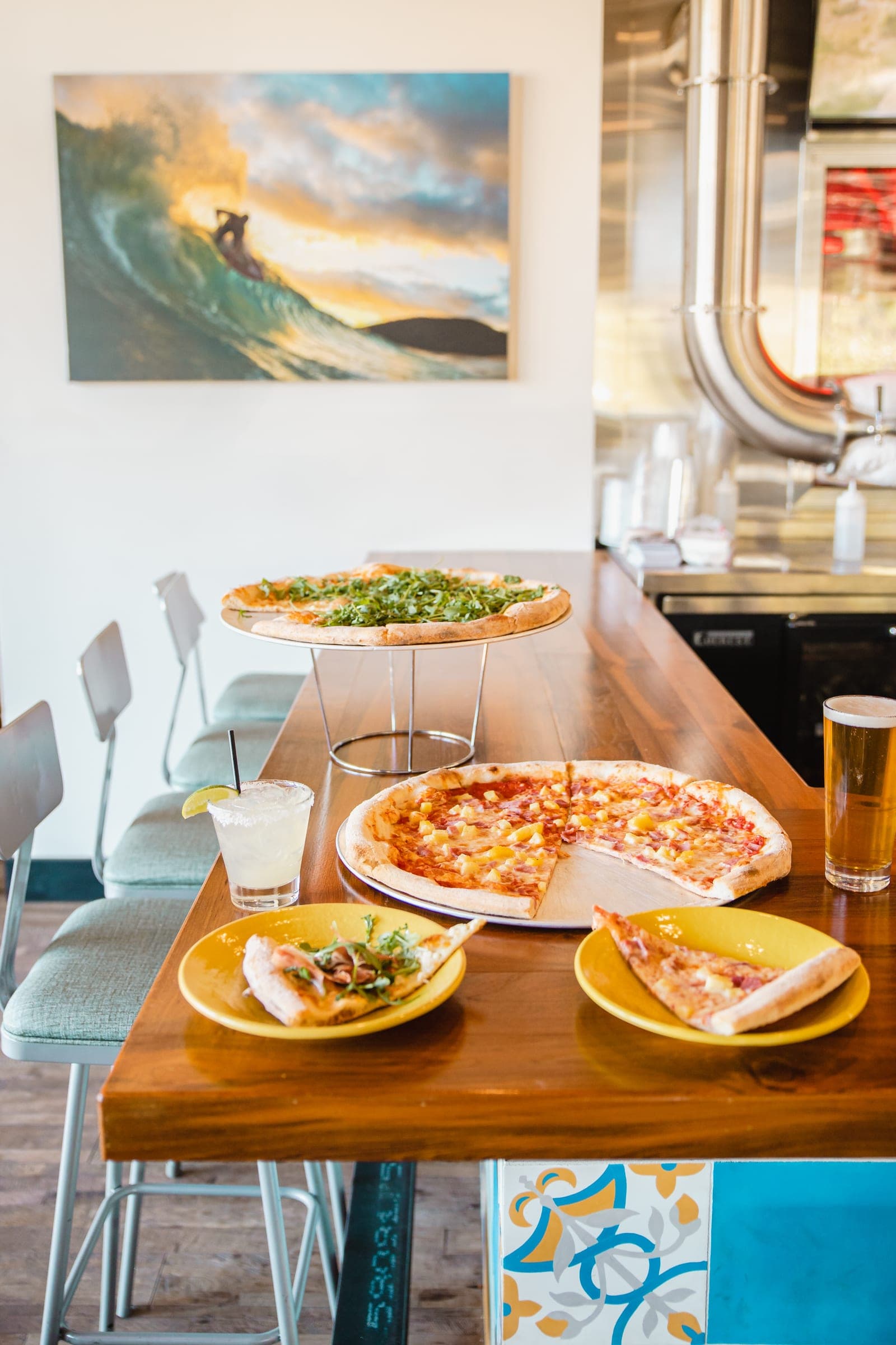 Two pizzas on a Best Pizza & Brew bar table beside a pint of beer and a margarita