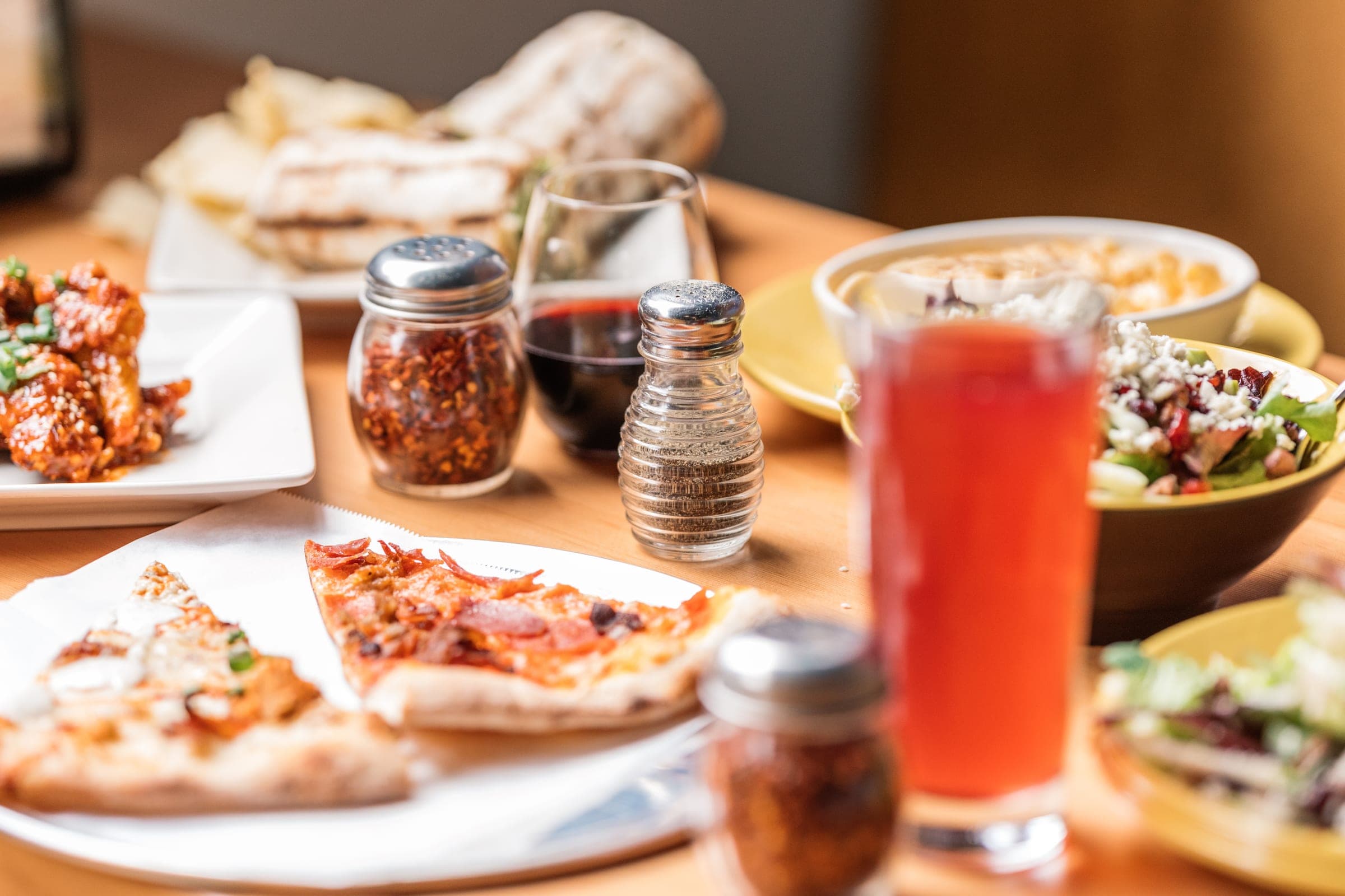 Pizza slices, glazed wings and a chopped salad shared across a table during a fundraiser night
