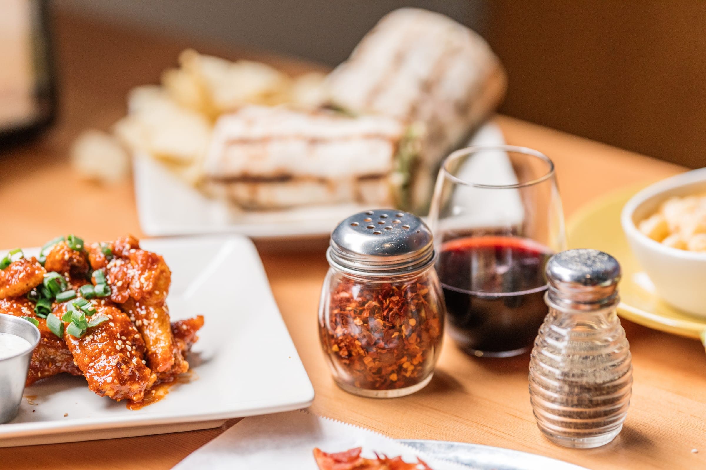 Glazed wings, a grilled wrap and a glass of red wine on a shared table