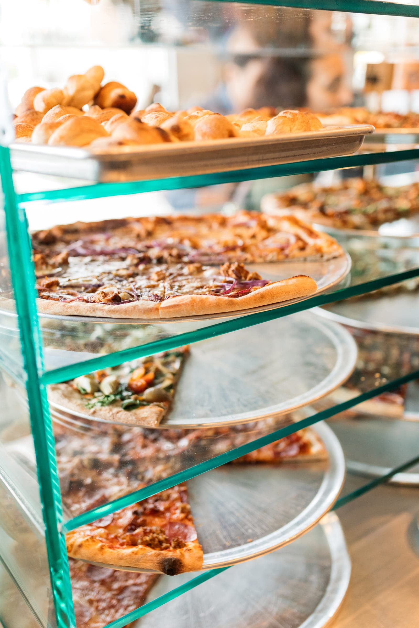 Whole pizzas lined up in the by-the-slice display case