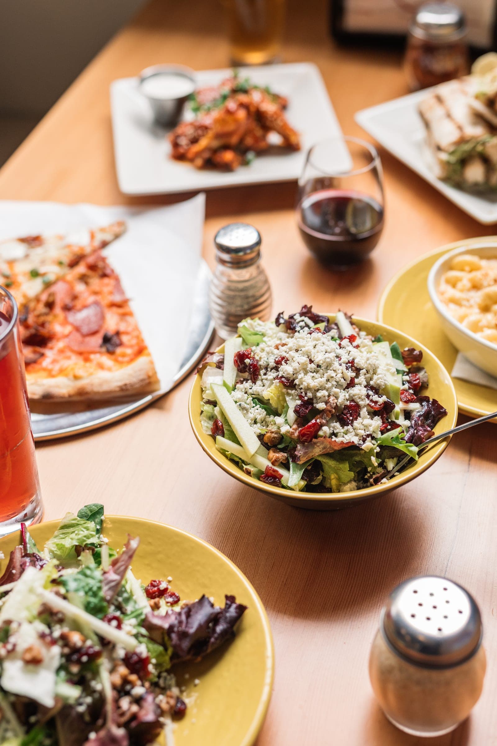 A table spread of pizza slices, a chopped salad and drinks at Best Pizza & Brew