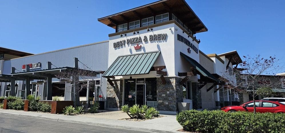Best Pizza & Brew Carmel Mountain from the parking lot, its signed corner tower and green awnings above a stone facade under a clear sky