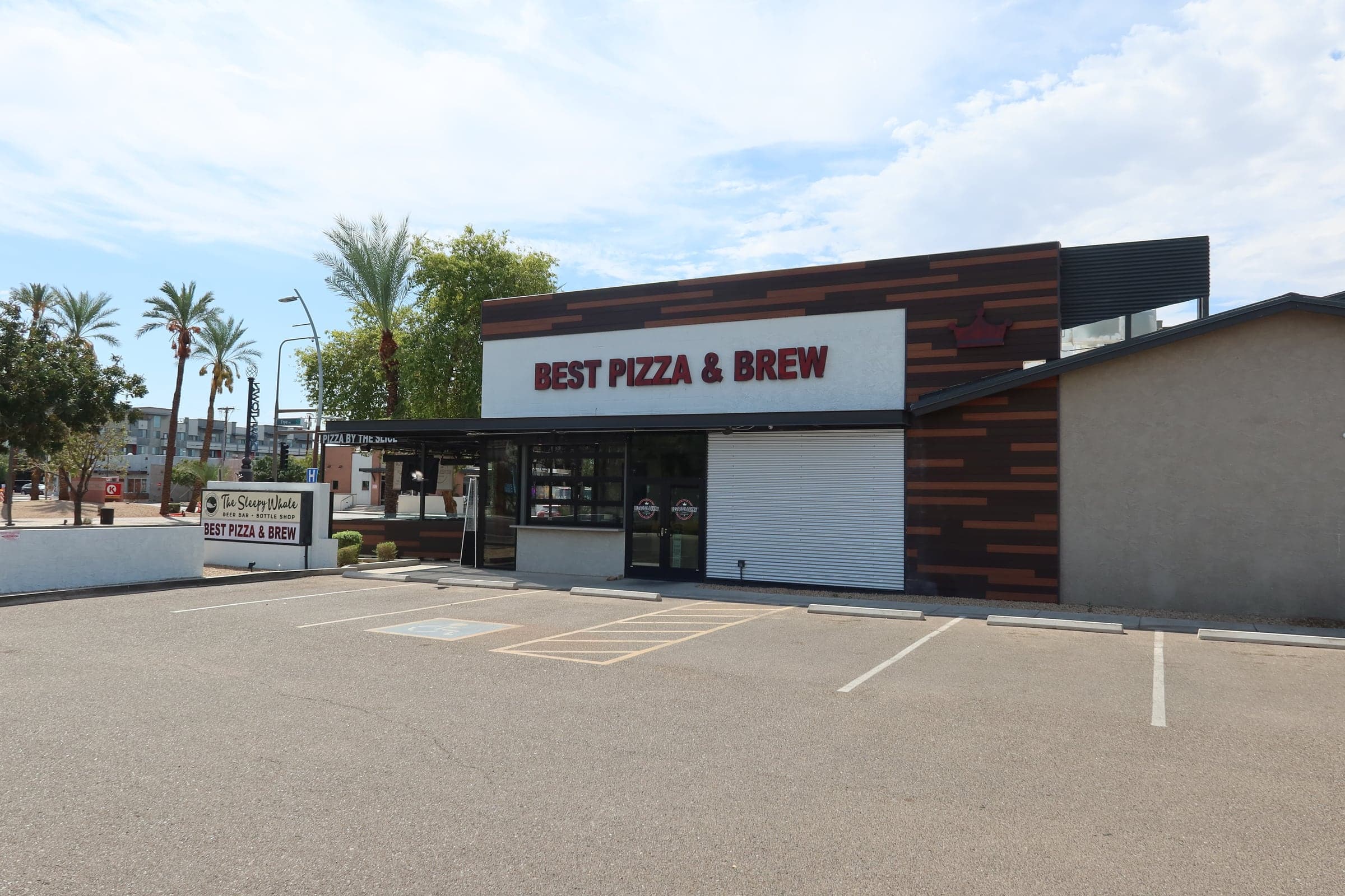 Best Pizza & Brew Chandler, Arizona, seen across its parking lot: a timber-clad storefront with the name in red above the entrance and palms behind it
