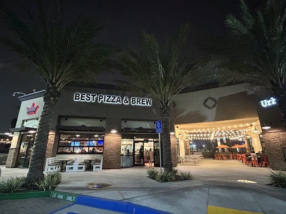 Best Pizza & Brew Clairemont at night, its lit sign glowing between palm trees above a string-lit patio