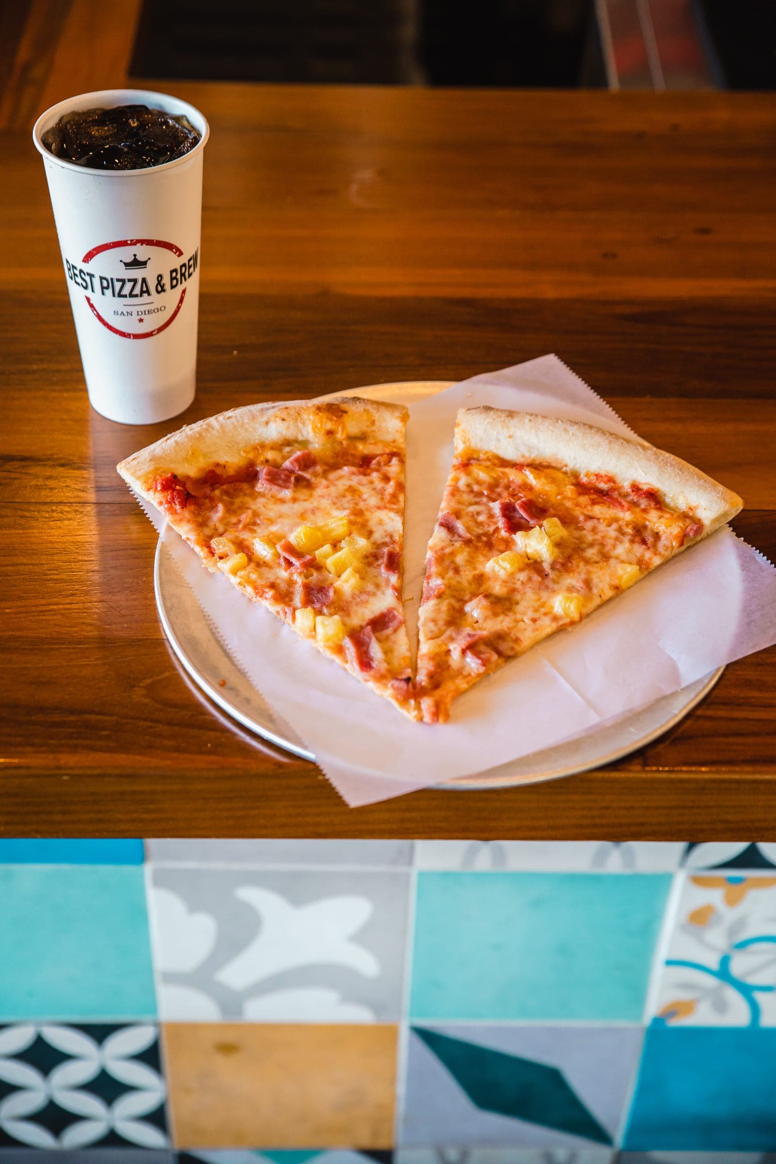 Two pizza slices on a tray beside a Best Pizza & Brew fountain drink